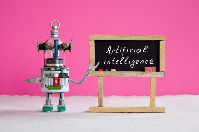 Photo of a toy robot pointing to a sign that says "Artificial Intelligence"